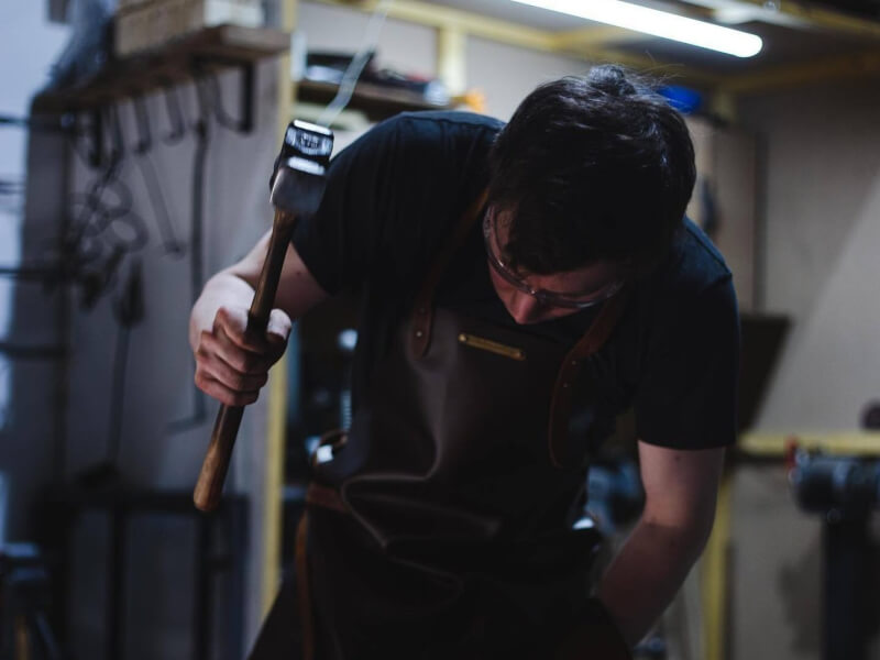 A man at a blacksmithing class is hitting white hot metal with a hammer